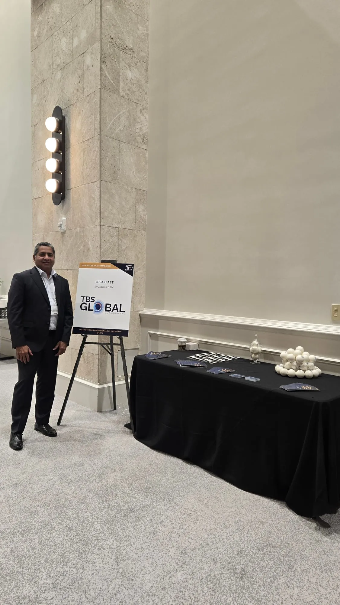 The TBS Global breakfast sponsorship sign and information table in the symposium foyer